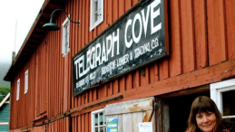 photo from telegraph cove with red building and Kate standing beside it
